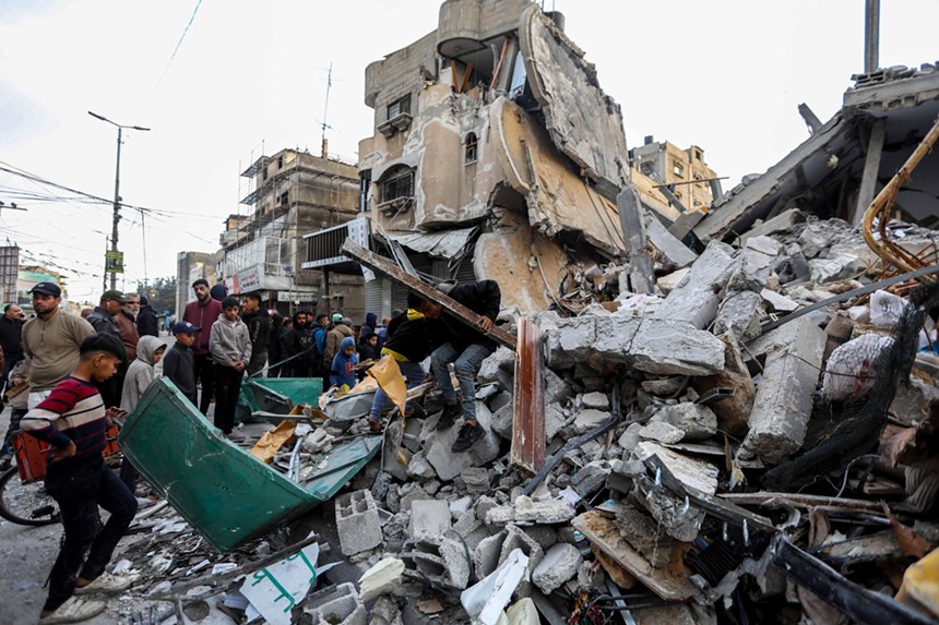 In Rafah, a group of residents stand around a massive pile of rubble left after an Israeli airstrike