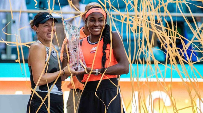 Color photo of two smiling women's tennis professionals holding a glass trophy