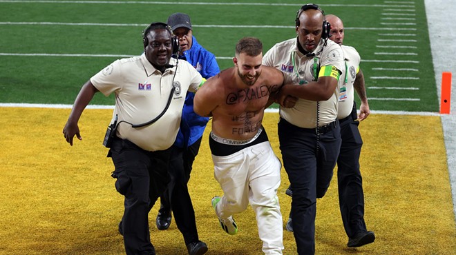 A shirtless Super Bowl streaker smiles as security guards haul him off the Allegiant Stadium turf.