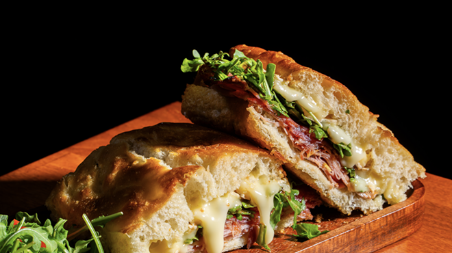 An Italian sandwich with cheese and arugula on a wooden platter
